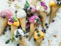 Bunte Eistüten mit Blaubeeren und Blüten. Wer fragt sich, wie viel Kalorien hat eine Kugel Eis, wenn sie so verlockend aussieht?