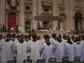 Młodzi mężczyźni w białych szatach, przygotowujący się do bierzmowania, stoją przed bazyliką.