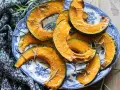 Fette di zucca in friggitrice ad aria, dorate e profumate al rosmarino, servite su un piatto blu e bianco.