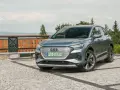 Szary Audi Q4 na kamienistym podjeździe, z widokiem na góry i las.