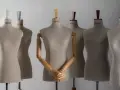 Kilka manekinów krawieckich w neutralnych kolorach, jeden z drewnianymi rękami złożonymi na piersi.
