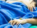 Ręka pacjenta z wenflonem pod niebieskim kocem, walczącego z wstrząsem septycznym.