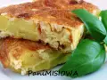 Pyszna tortilla de patatas, ze złotobrązową skórką i soczystym wnętrzem, ozdobiona świeżymi liśćmi bazylii.
