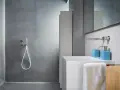 Bagno moderno con rivestimento doccia senza piastrelle effetto resina, lavabo bianco e accessori azzurri.