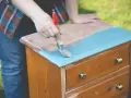 Persona pinta con brocha azul una mesita de noche de madera, transformándola en una de las mesitas de noche pintadas a la tiza.