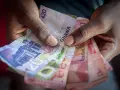 Dłonie trzymające banknoty cedi Ghany o różnych nominałach.