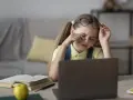 Zmęczona dziewczynka z okularami na czole pociera oczy, ucząc się przy laptopie. Jej indywidualna ścieżka nauczania jest trudna.