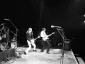 Deux guitaristes d'un groupe français rock jouent sur scène, éclairés par des projecteurs.