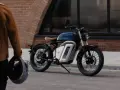 Eleganckie motocykle retro w miejskiej scenerii. Mężczyzna w brązowej kurtce trzyma kask, gotowy do jazdy.