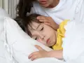 Chore dziecko w łóżku, mama głaszcze je po czole. Warto pamiętać o odpowiednich paracetamol czopki dawki dla dzieci.