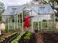 Frau mit Huhn vor Gewächshaus, daneben junge bauerngarten pflanzen.