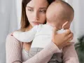 Traurige Mutter hält ihr Baby. Ihre Augen spiegeln eine tiefe Enttäuschung wider, vielleicht gender disappointment.