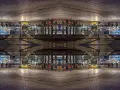 Nocne miasto z żółtym tramwajem i ludźmi. Kompozycja symetryczna tworzy surrealistyczny, odbity świat.