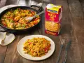 Paella de carne recién hecha en sartén y plato, lista para disfrutar. Un caldo Gallina Blanca para paella fácil de carne a su lado.
