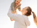 Mutter wirft ihr lachendes Baby in die Luft. Ein fröhlicher helikopter-mutter test im Freien.