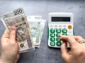Ręka z polskimi banknotami 200 zł i 100 zł obok kalkulatora z wyświetloną kwotą 50000. Planowanie waloryzacji emerytury 2026.