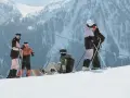 Grupa narciarzy i snowboardzistów odpoczywa na stoku, podziwiając majestatyczne góry Sierra Nevada.