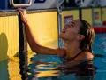 Nuotatrice con gocce d'acqua sul viso, aggrappata al bordo giallo della piscina. Si può fare il bagno in piscina con il ciclo, senza problemi.