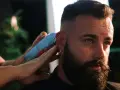 Un hombre con barba y aros en las orejas recibe un corte de pelo moderno, anticipando las tendencias de corte de pelo hombre 2026.