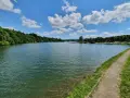 Ein sonniger Tag am Ellwanger See mit bewaldeten Ufern und einem Weg am Wasser.