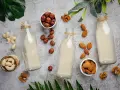 Deser chia na mleku kokosowym czy krowim? Butelki z mlekiem roślinnym, orzechy laskowe, migdały, orzechy włoskie i nerkowce.