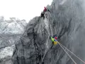 Wspinaczka na Piramidę Carstensza. Alpinista z plecakiem zjeżdża po linie, podczas gdy inni czekają na szczycie.