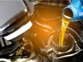 Olio giallo versato da una bottiglia blu in un motore. La differenza tra olio sintetico e minerale è fondamentale per la salute del motore.
