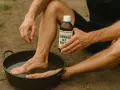 Un homme utilise un produit pour comment durcir la peau des pieds, trempant un pied dans une bassine d'eau.