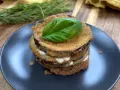 Deliziose cotolette di melanzane impilate, farcite con formaggio cremoso e guarnite con una foglia di basilico fresco.