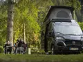 En solig dag med en clever sunny 540 husbil parkerad i skogen. Tre personer sitter vid ett bord och njuter av naturen.