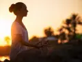 Frau meditiert im Sonnenuntergang. Ein kurzer 5-Minuten-Meditations-Text könnte hier perfekt passen, um diese friedliche Szene zu vertiefen.