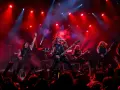Un groupe metal actuel enflamme la scène sous des projecteurs rouges. Les musiciens jouent avec passion, leurs cheveux volant au vent, devant une foule en délire.