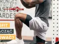 Mężczyzna w stroju sportowym wykonuje ćwiczenie CrossFit przy stojaku gimnastycznym.