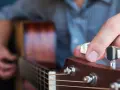 Dłoń stroi gitarę, kręcąc kluczem, by uzyskać idealny dźwięk E.