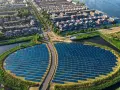 Un grande campo di pannelli solari, simbolo di rigenerazione urbana significato, circonda un quartiere residenziale con case moderne e canali.