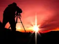 Silhouette d'un photographe sur trépied, capturant le soleil éclatant lors d'un coucher de soleil rougeoyant.