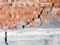 Pęknięta ceglana ściana i betonowy cokół, wskazujące na podbijanie fundamentów.