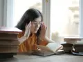 Ragazza con occhiali e mani sulle tempie, circondata da libri. Potrebbe soffrire di mancanza di concentrazione cause.