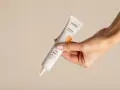 Dłoń trzyma tubkę kremu z filtrem SPF 50+, idealnego do codziennej pielęgnacji. To kwintesencja skinimalizmu – prostota i skuteczność.