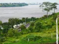 Droga wije się przez zielone wzgórza w kierunku stolicy DRK, z szeroką rzeką i panoramą miasta w oddali.