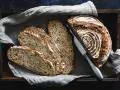 Ein rustikales Roggenbrot, in Scheiben geschnitten, liegt in einer Holzkiste auf Leinentuch. So vielseitig, was man aus Roggen machen kann!