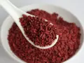 Un cucchiaio bianco pieno di riso rosso fermentato, ingrediente noto per il suo effetto sul gonfiore addominale.