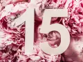 Białe cyfry "15" na tle bujnych, różowych piwonii. Symbolizują 15 rocznicę ślubu, pełną miłości i piękna.