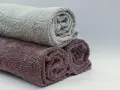 Trois serviettes de bain roulées, une grise et deux prune, prêtes à être cousues pour un projet de couture.