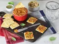 Pyszna pasta z suszonych pomidorów na krakersach, obok miseczka orzechów i szklanka wody. Idealna przekąska!