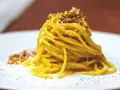 Un piatto di spaghetti alla carbonara fumante, guarnito con pecorino e pepe nero.