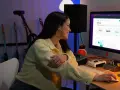 Junge Frau am Computer, die Statistiken für digitalen Musikvertrieb prüft. Gitarren im Hintergrund.