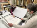 Deux personnes manipulent un dessin au crayon, peut-être un portrait, sur une table. Le vernis protège l'œuvre.