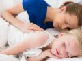 Mama i dziecko śpią razem, otuleni białymi pościelami. Czy dzieci powinny spać z rodzicami? Ta chwila spokoju sugeruje, że tak.