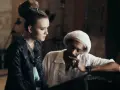 Snoop Dogg w białej koszuli i beretce Rasta, rozmawiający z młodą kobietą. Może to być scena z jednego z jego **snoop dogg utworów**.